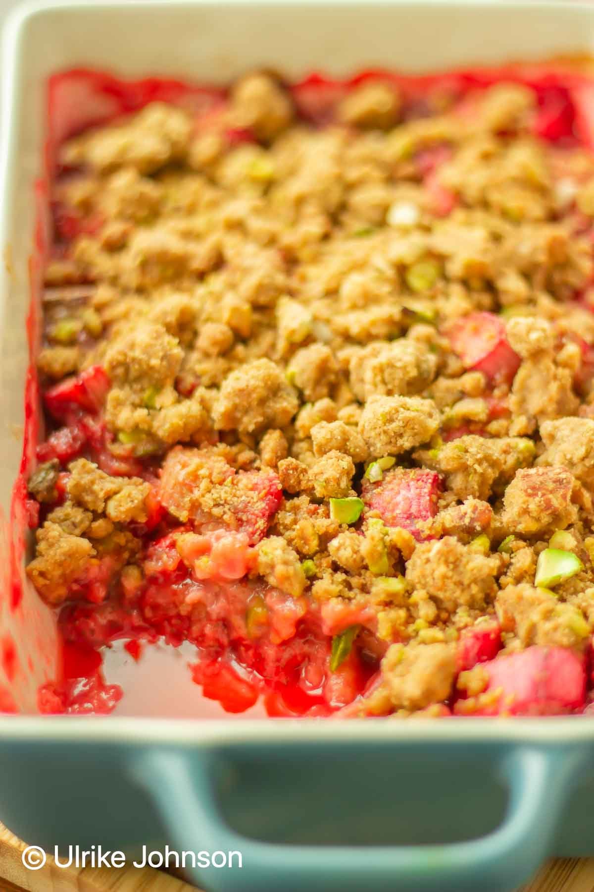 Strawberry Rhubarb Crumble with pistachio streusel topping in a blue casserole dish