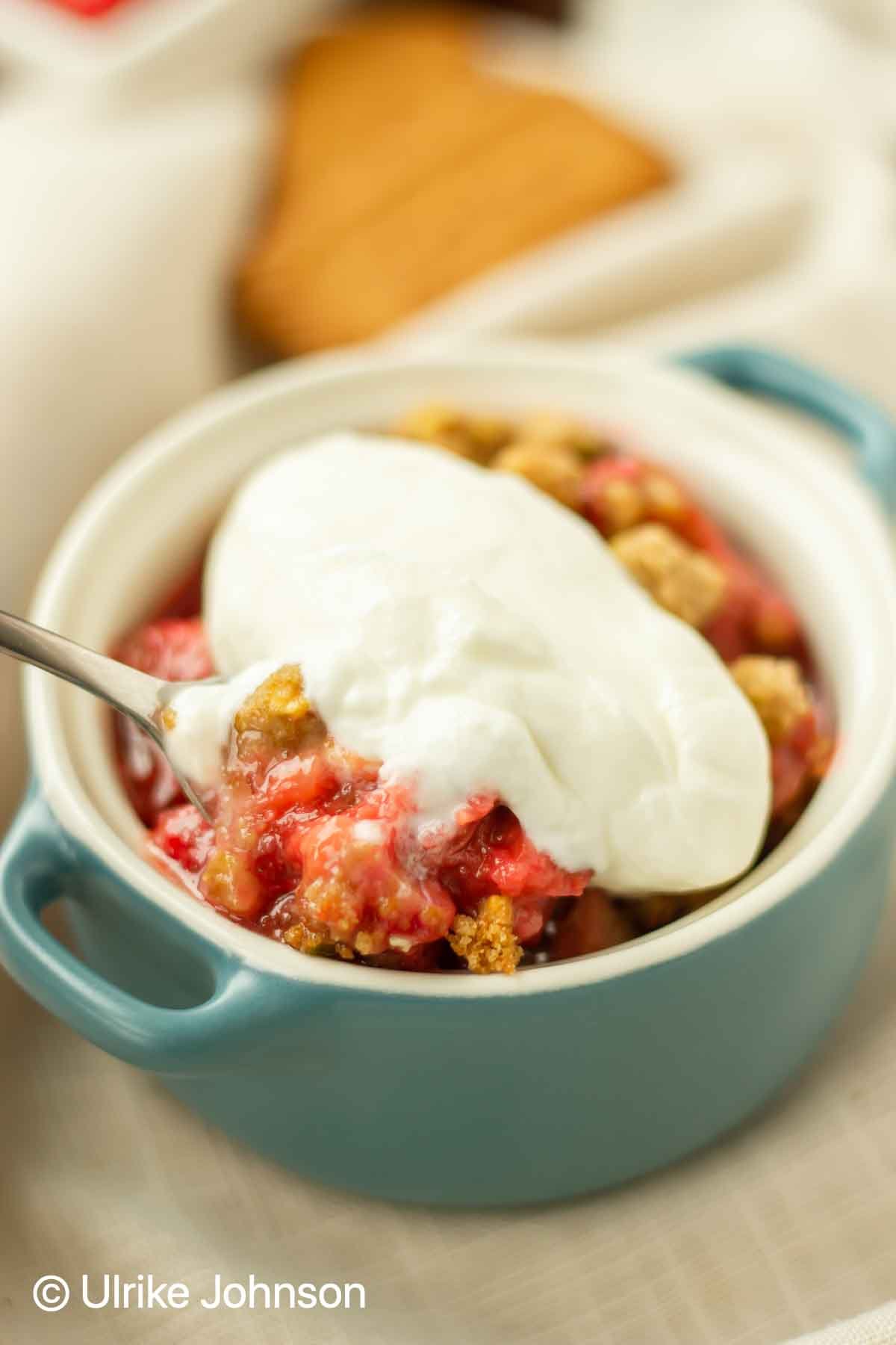 old-fashioned strawberry rhubarb crumble with pistachio streusel topping served in a small blue casserole dish 