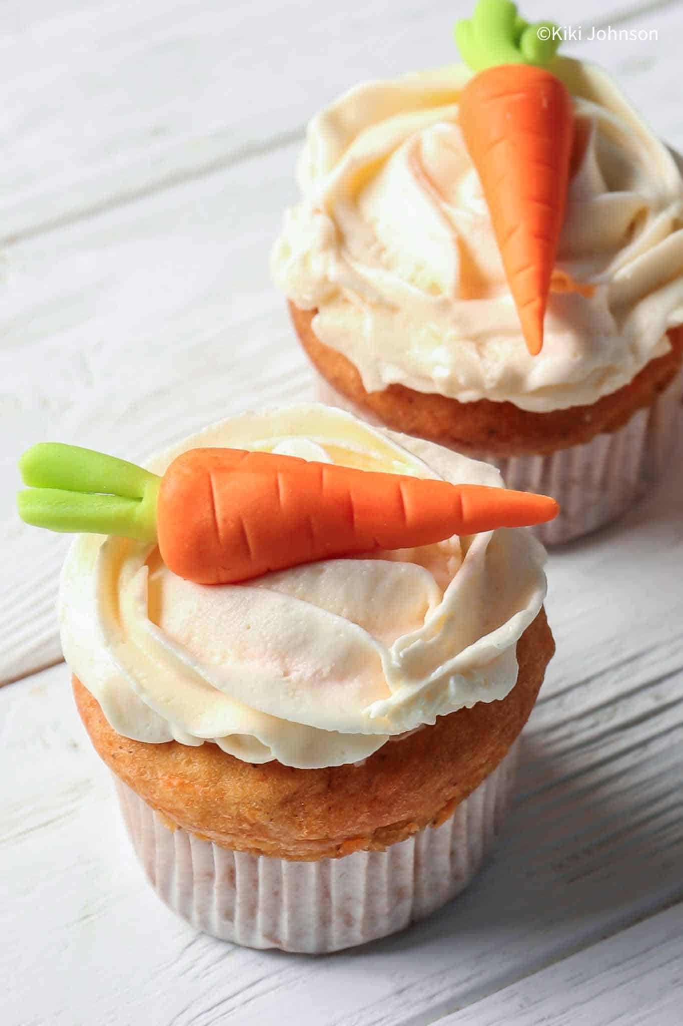 two carrot banana muffins topped with German quark frosting and marzipan carrots