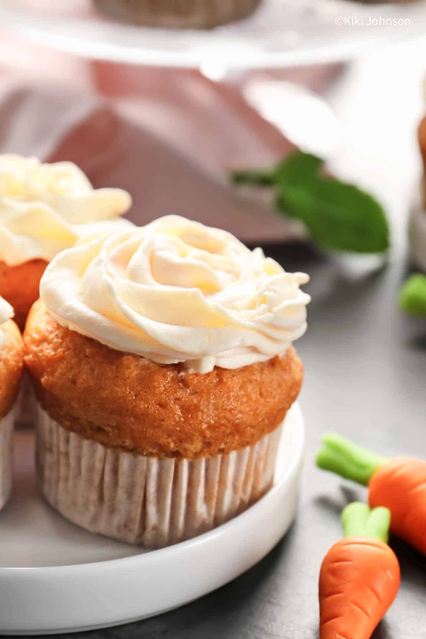 a moist carrot banana muffin topped with a swirl of quark frosting with some marzipan carrots on the side