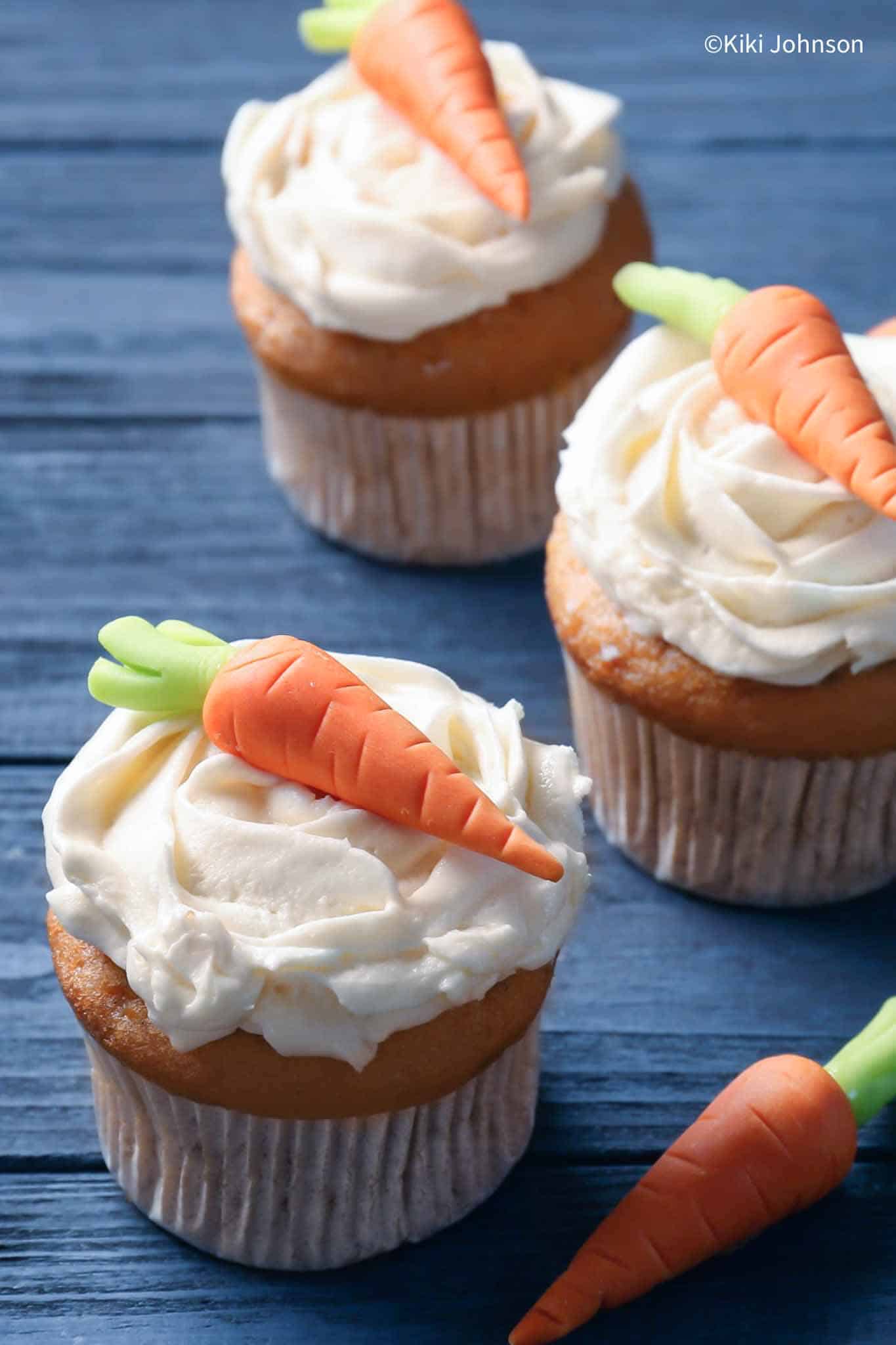 three banana carrot cake muffins topped with quark frosing and decorated with sugar carrots