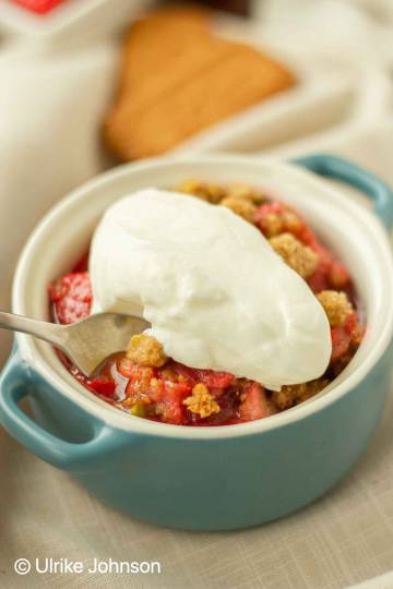 strawberry rhubarb crumble served with a dollop of cream in a small blue dish