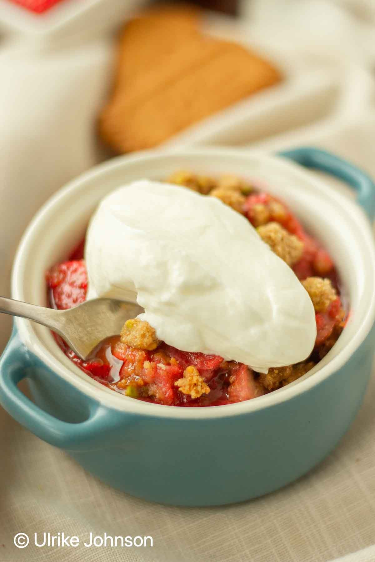 a serving of strawberry rhubarb crumble served with a dollop of whipped cream in a small blue baking dish