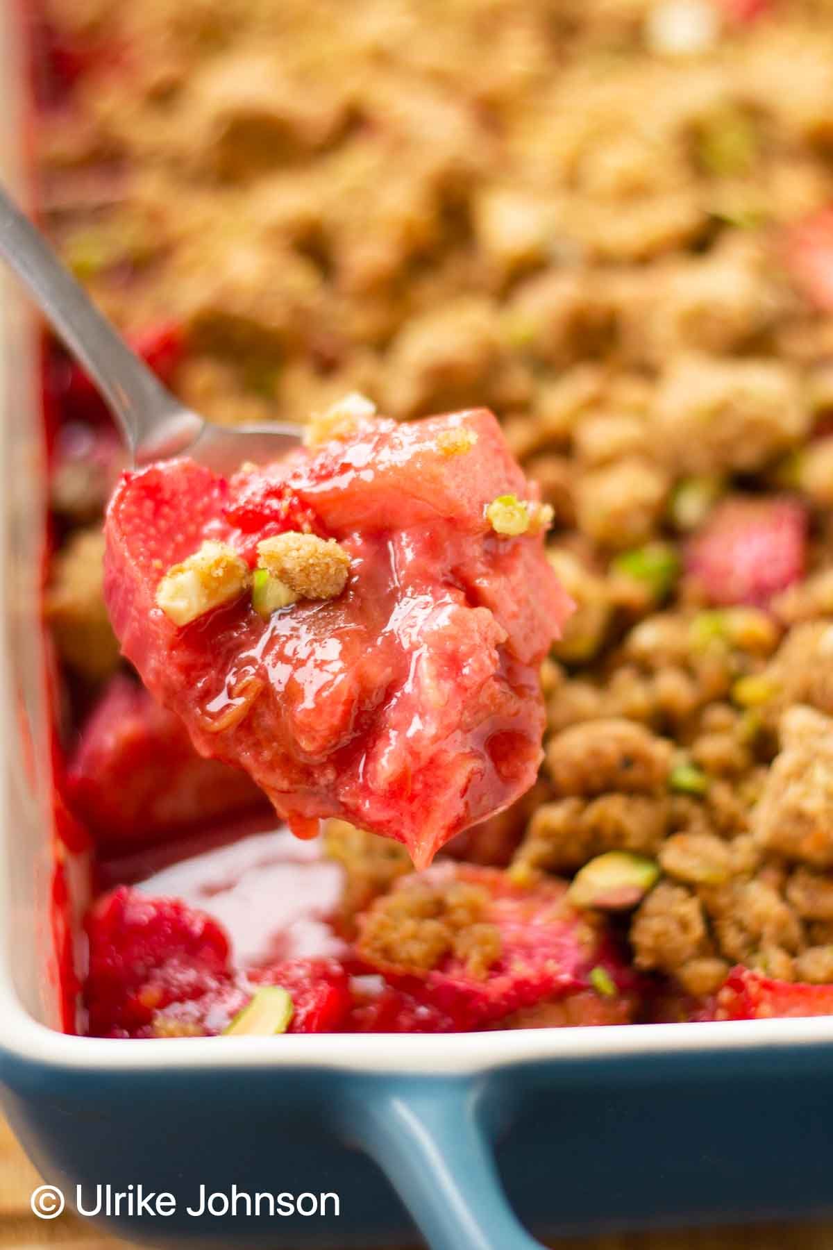 a spoon of strawberry rhubarb crumble with perfect crumble topping with pistachio nuts