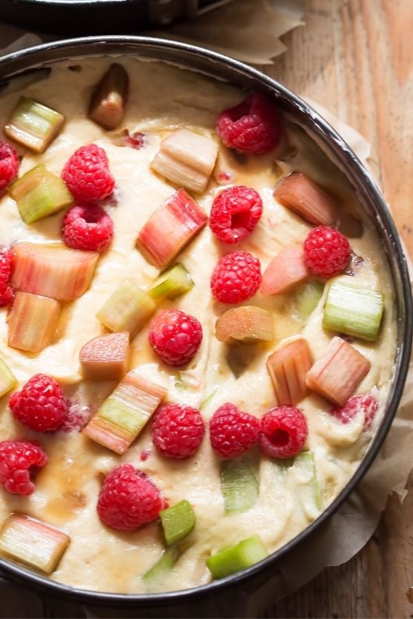 a springform pan with cake batter topped with raspberries and rubarb