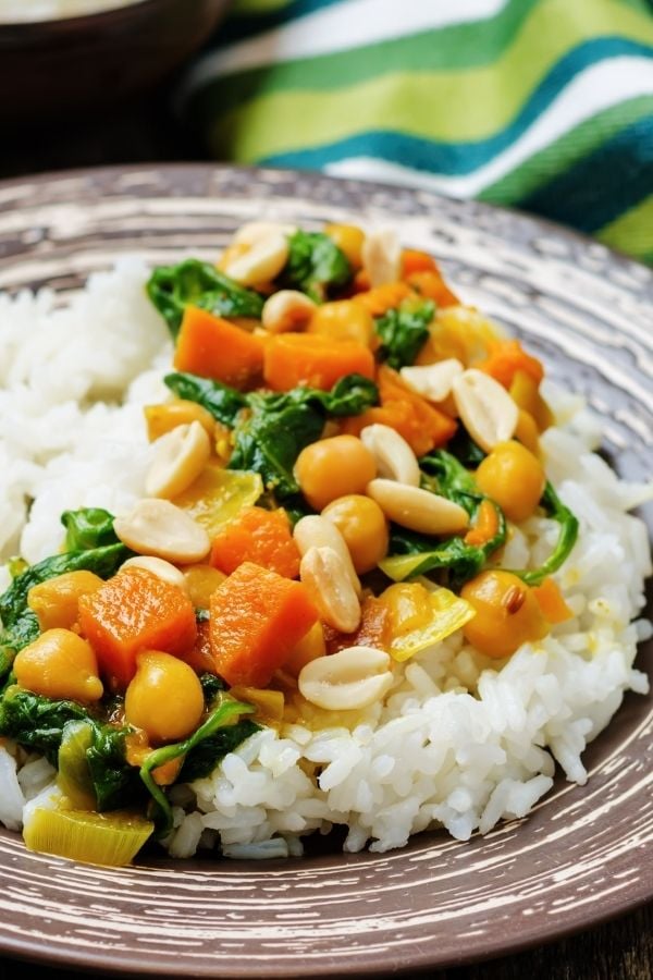 creamy vegan chickpea curry with pumpkin, spinach and chopped peanuts served over rice