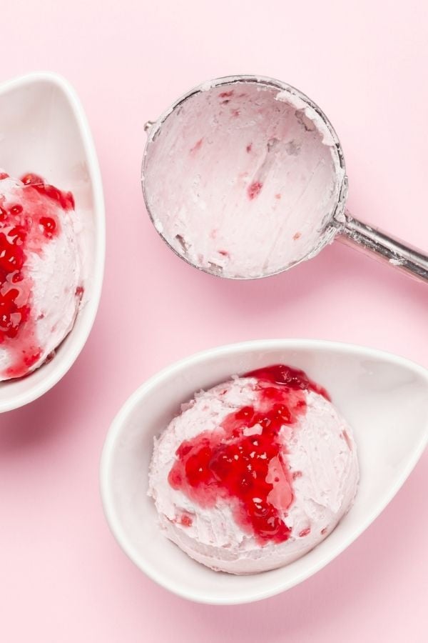 a scoop of raspberry coconut milk ice cream in a small bowl with an ice cream scoop on the side