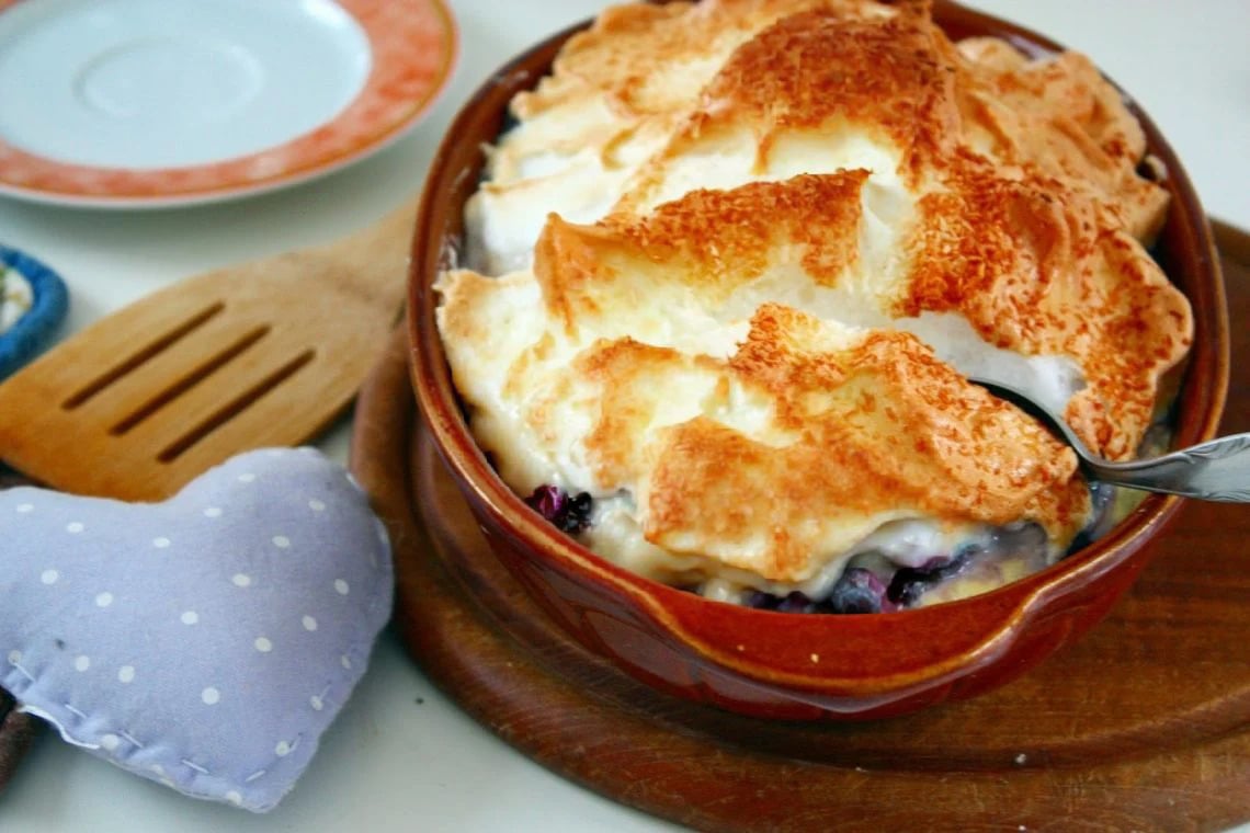 baked rice pudding with blueberries and topped with meringue topping in a brown casserole dish.