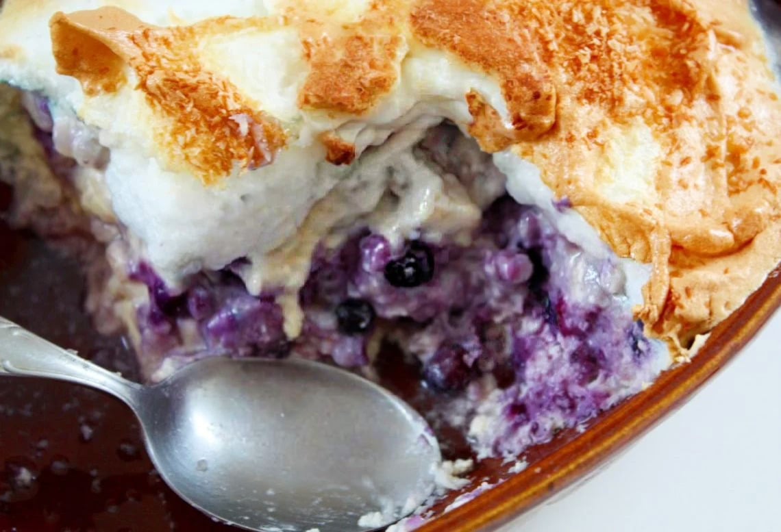 a casserole dish with baked coconut blueberry rice pudding topped with meringue 
