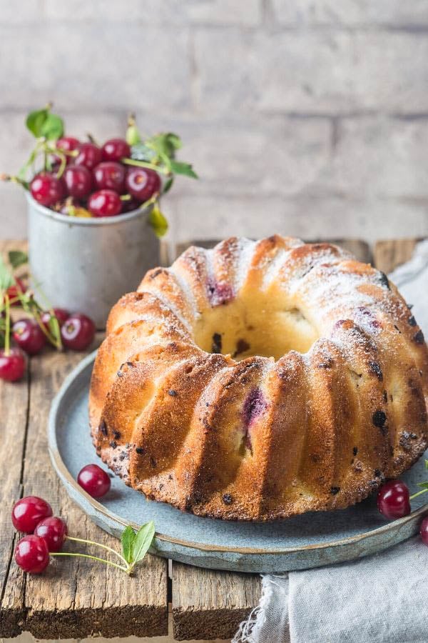 an easy White Chocolate Cherry Bundt Cake on a pale blue platter with fresh sour cherries in the background 