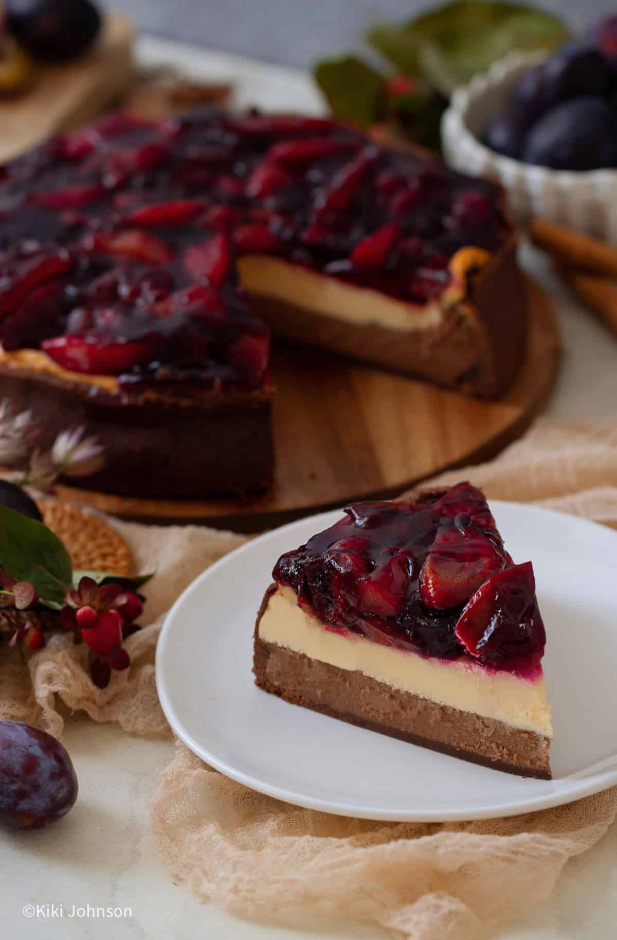 ein Stück Schoko Vanille Käsekuchen mit Portwein Zwetschgen Topping auf einem weissen Kuchenteller