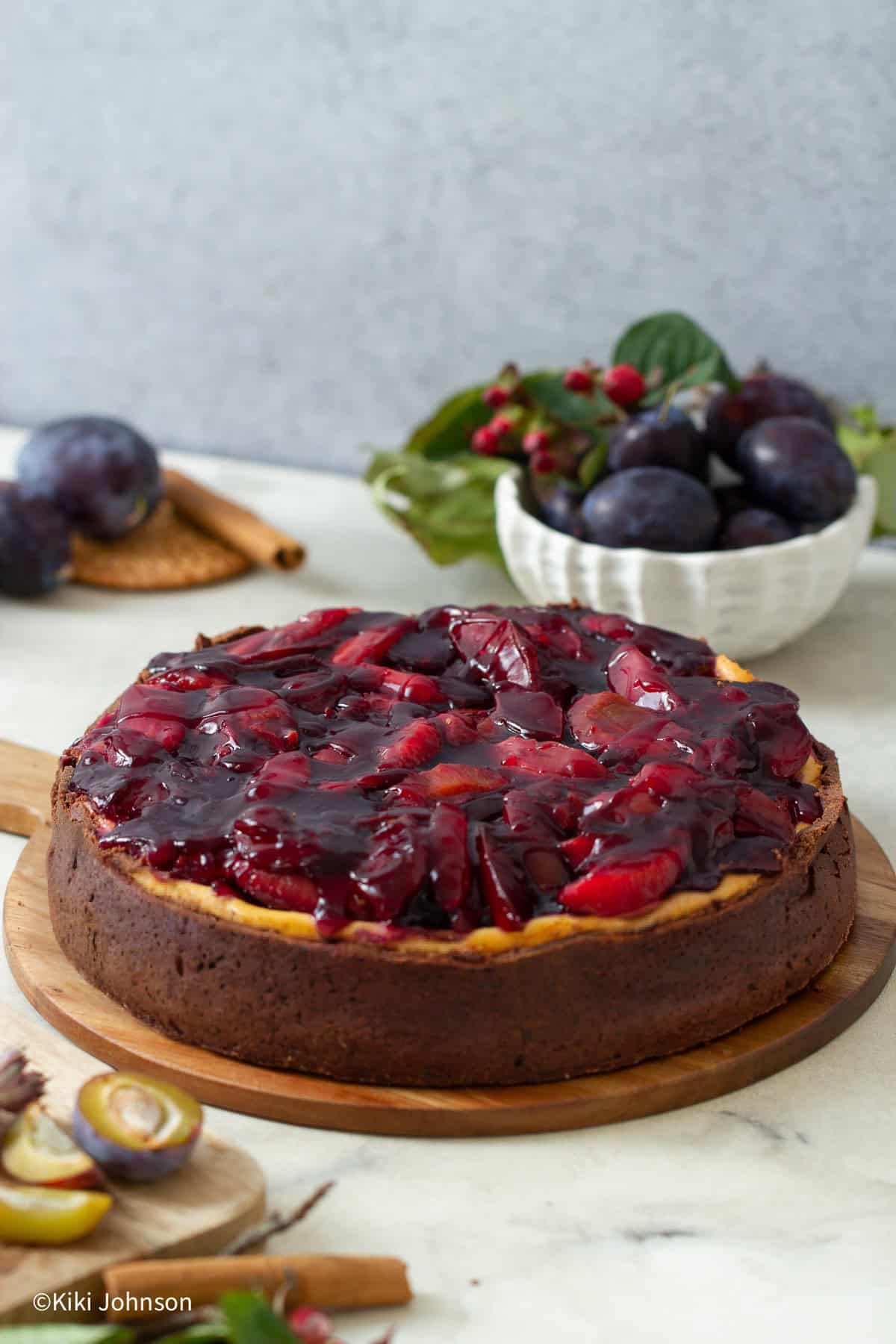 ein ganzer Schoko Vanille Käsekuchen mit Portwein Zwetschgen Topping auf einer Kuchenplatte aus Holz