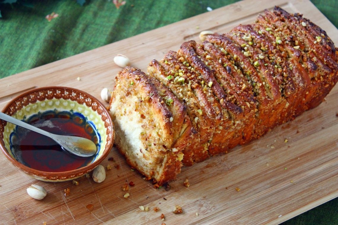 side view of a baklava pull-apart bread with honey syrup on the side