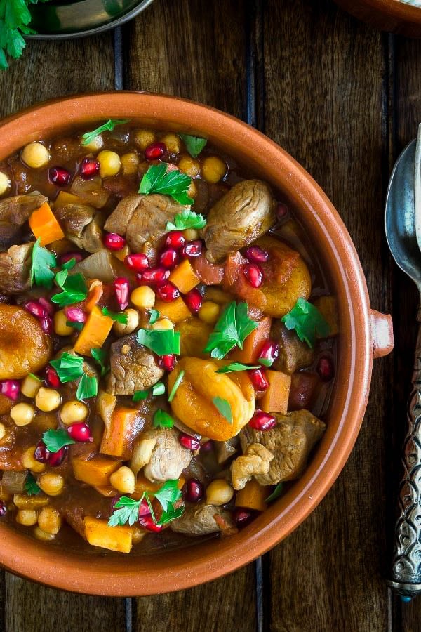 a clay bowl filled with Moroccan lamb tajine with pomegranate seeds and apricots 