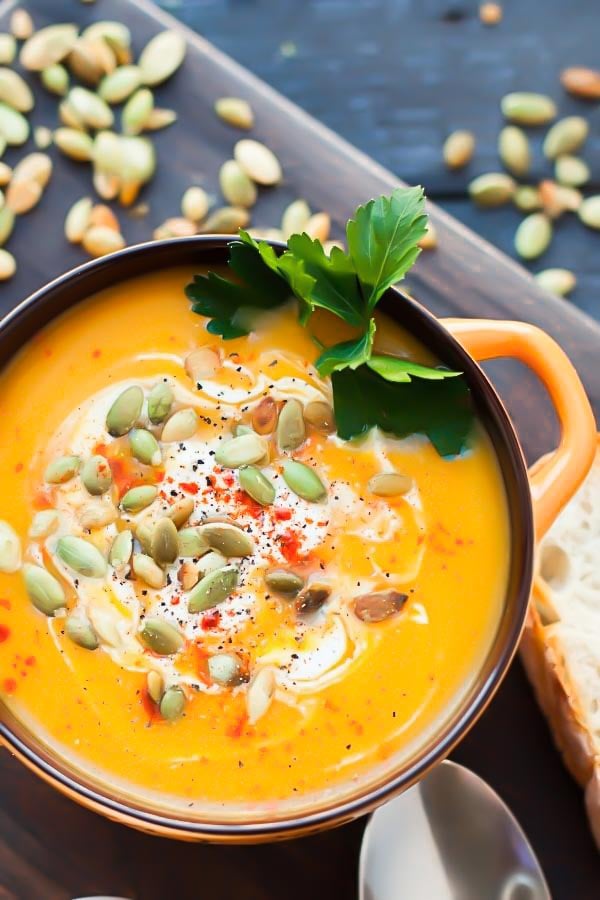 a small bowl with curried butternut squash soup topped with cream and pumpkin seeds 