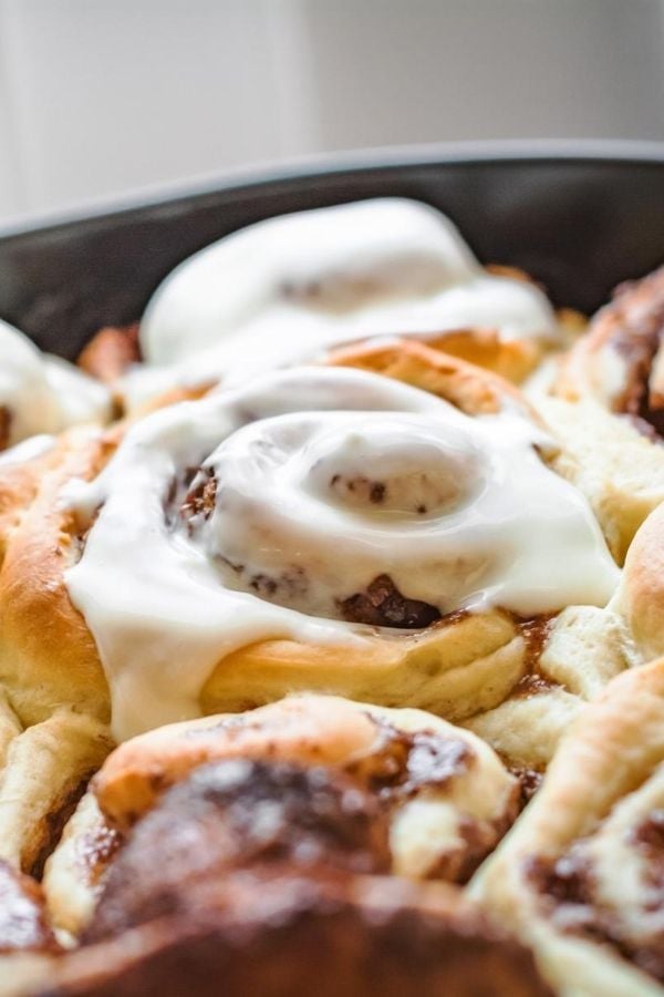 vegan banana cinnamon rolls in a black skillet drizzled with icing