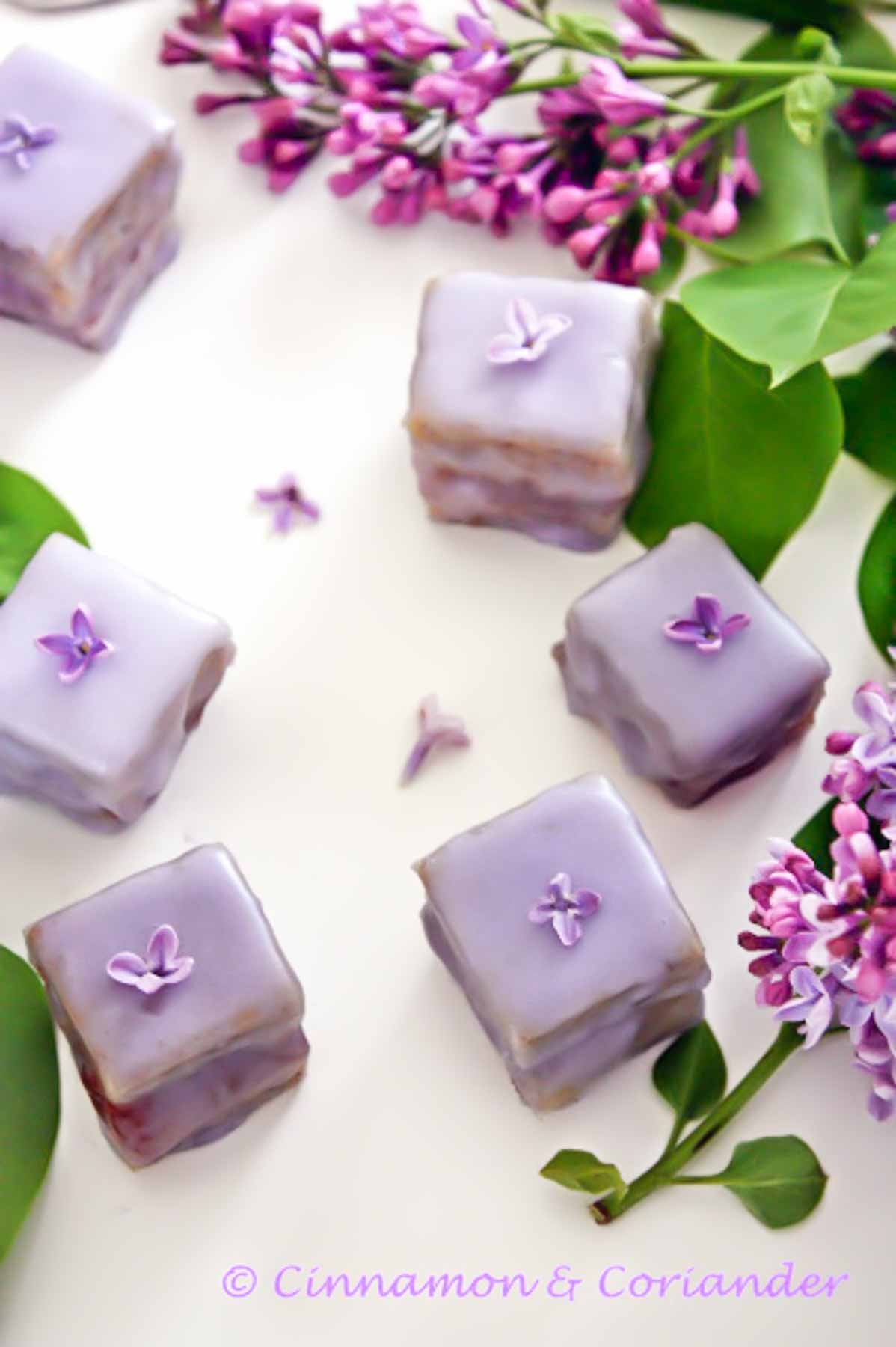 lilac petit fours with homemade lilac jelly and marzipan on a table surrounded with lilac flours