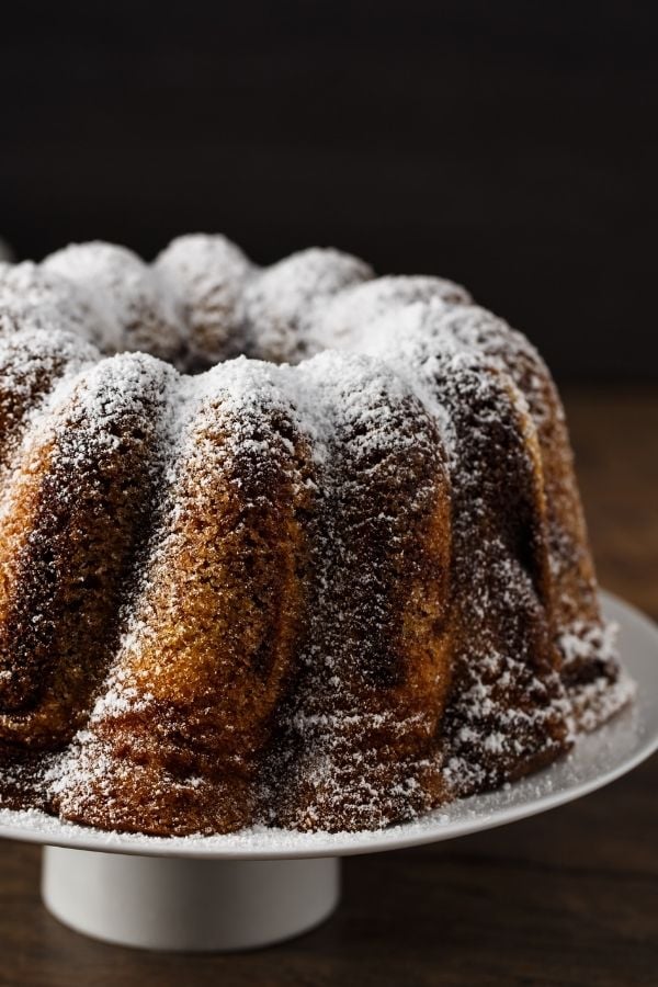 Omas Saftiger Nusskuchen auf einer Kuchenplatte mit Puderzucker serviert