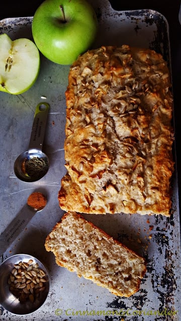 ein angeschnittenes Apfelbrot mit Rosmarin und Sonnenblumenkernen auf einem silbernen Blech.