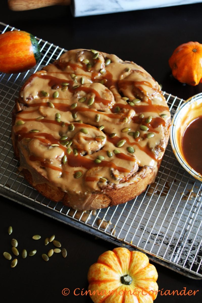 Pumpkin Pie Buns with Salted Caramel Glaze sprinkled with pepitas on a cooling rack