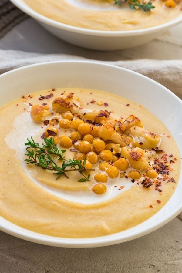 side view of a bowl of roasted cauliflower soup topped with cashew cream and chickpeas