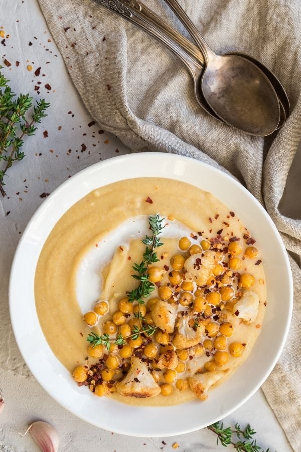 overhead shot of a bowl of creamy roasted cauliflower soup topped with chickpeas and cauliflower