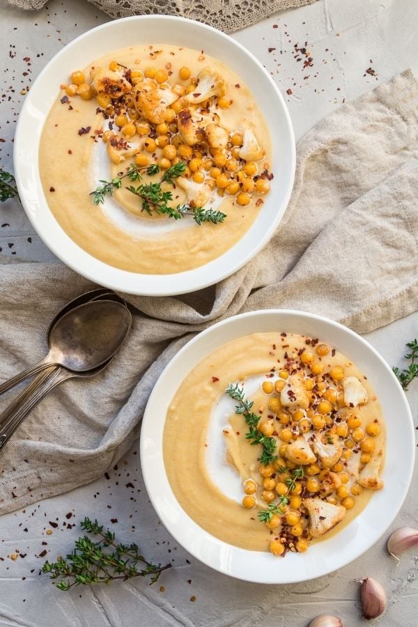 two bowls of vegan roasted cauliflower soup topped with chickpeas and cashew cream 