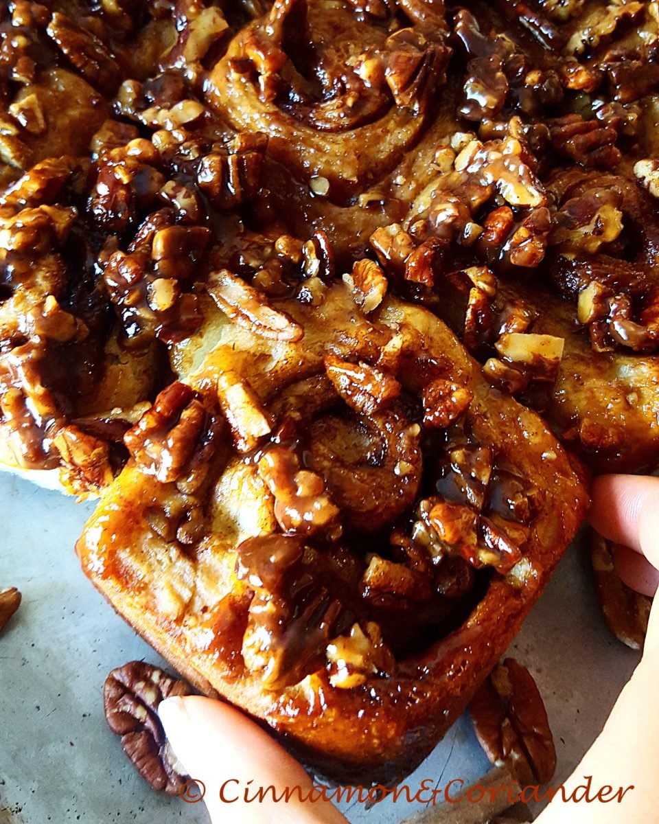 a hand reaching for the perfect fluffy caramel sticky bun with pecans on top
