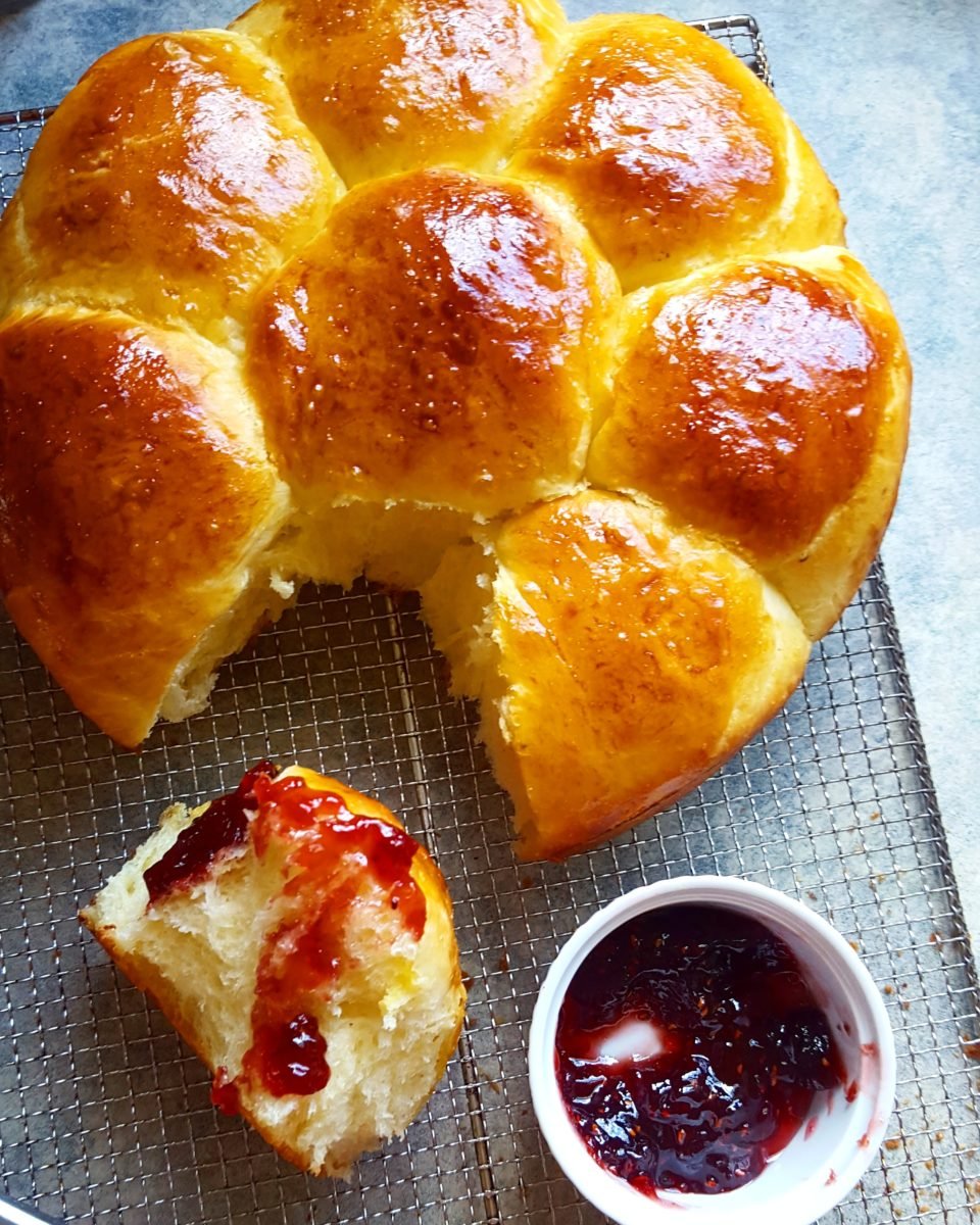 overhead shot of a loaf of brioche with one bun torn off and dipped into raspberry jam