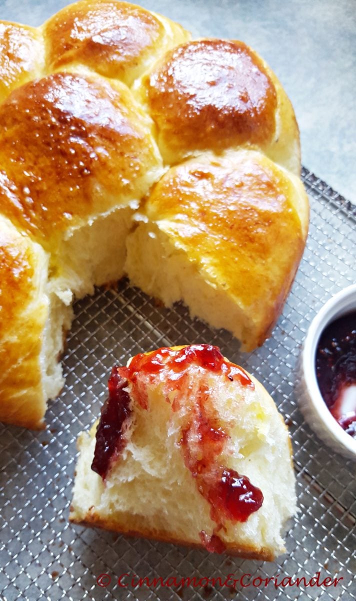 a tender brioche bun dipped into raspberry jam with a brioche loaf in the background