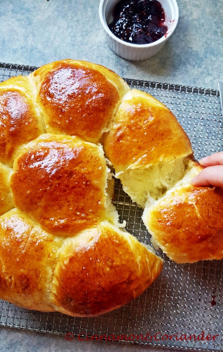 a hand tearing a brioche bun off a freshly baked brioche loaf