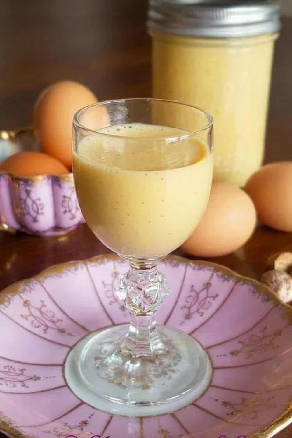 ein kleines Glas Eierlikör mit Eiern im Hintergrund 