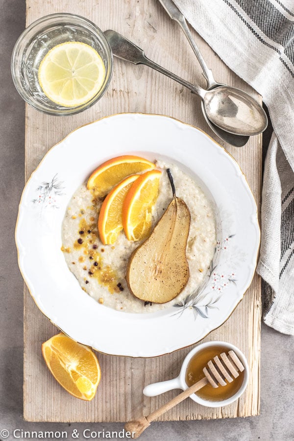 veganes Kokosmilch Porridge mit Birnen und Orangenscheiben auf einem Holzbrett serviert