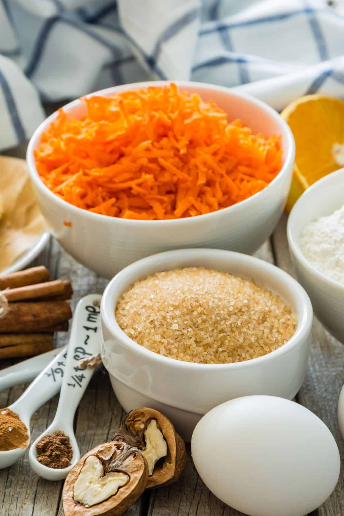 geriebene Karotten, Walnüsse, Eier und brauner Zucker und weitere Zutaten für Karottenkuchen auf einem Küchentisch