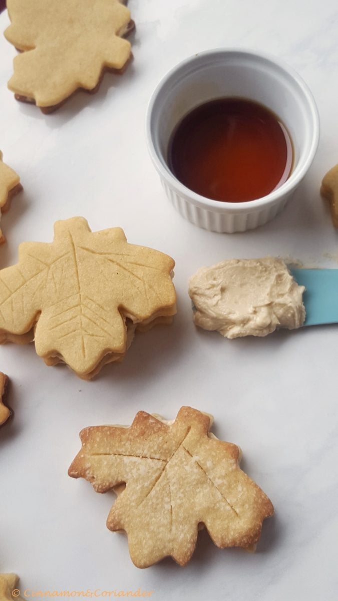 maple cream sandwich cookies on a marble countertop with maple buttercream on the side