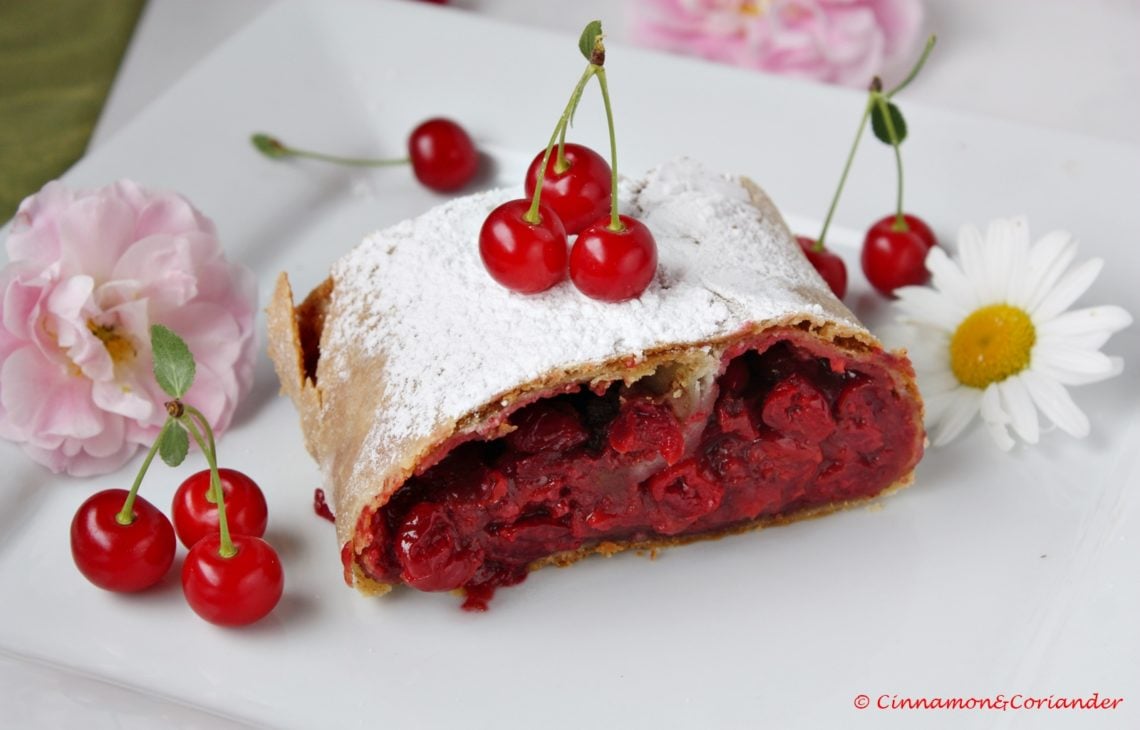 a slice of traditional sour cherry strudel dusted with icing sugar on a white plate
