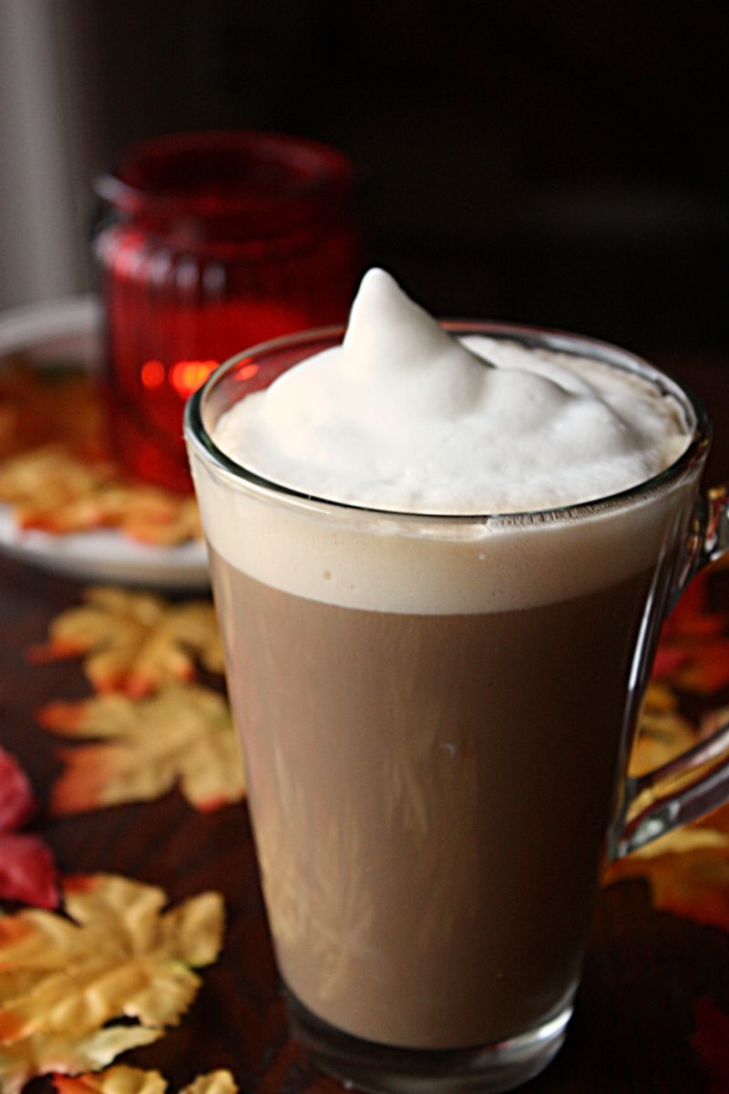 kanadisches Getränk Maple Latte in einem Glas mit reichlich Milchschaum und Herbst Deko im Hintergrund