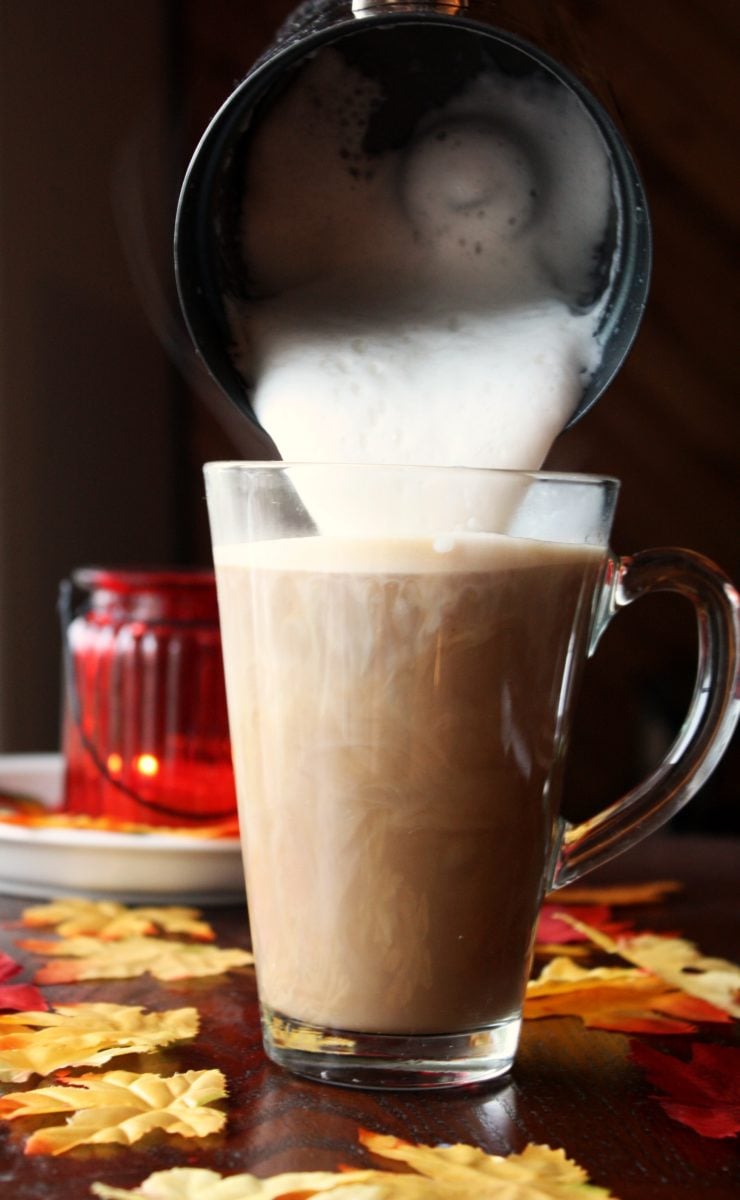 foamed milk being poured into maple flavored espresso in a tall glass mug