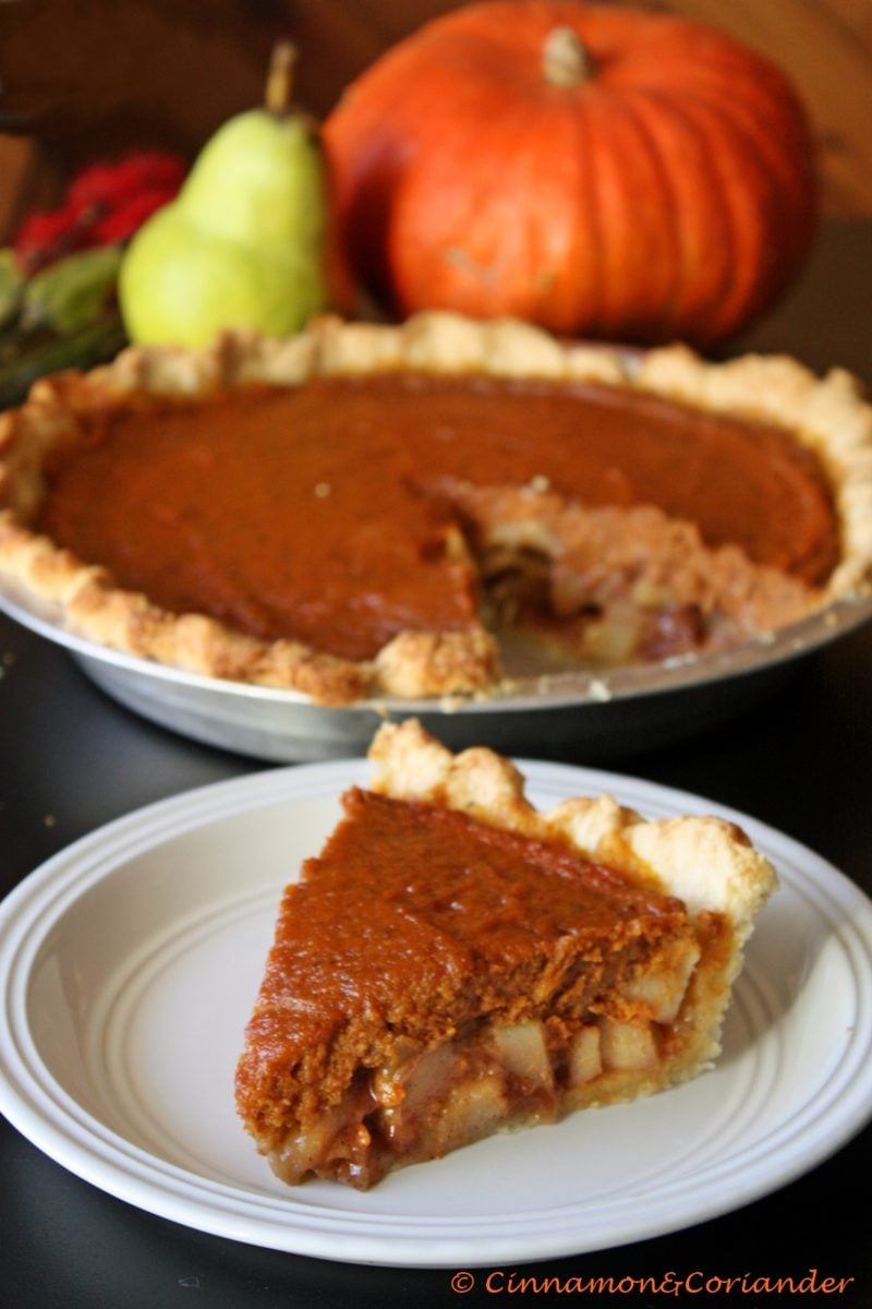 a slice of Caramel Pear Pumpkin Pie with homemade pumpkin pie filling served in a white plate with a whole pie and some pears and pumpkin in the background