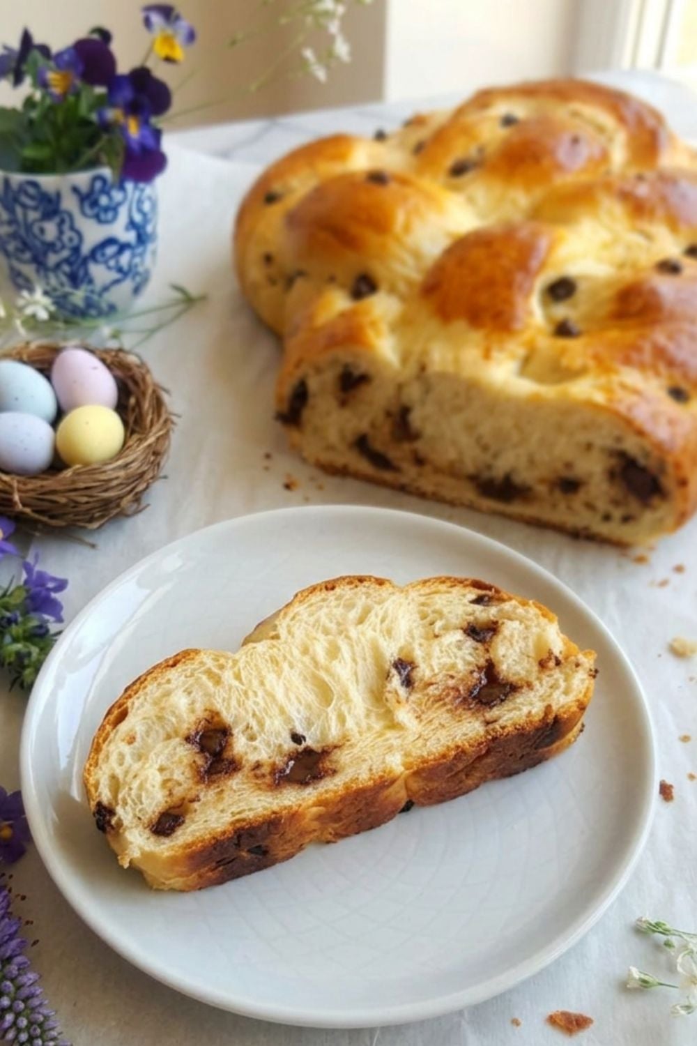 ein Stück Brioche Hefezopf mit Schokostückchen auf einem Oster Brunch Tisch mit Oster Eiern