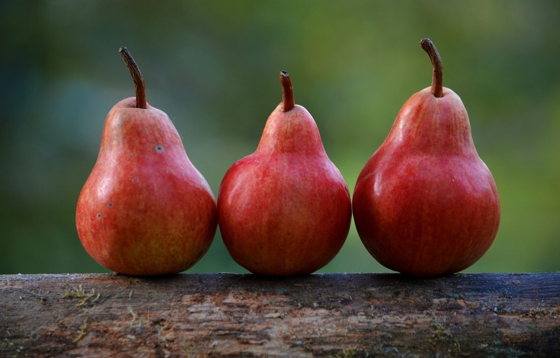 three red pears lined up on a piece of wood 