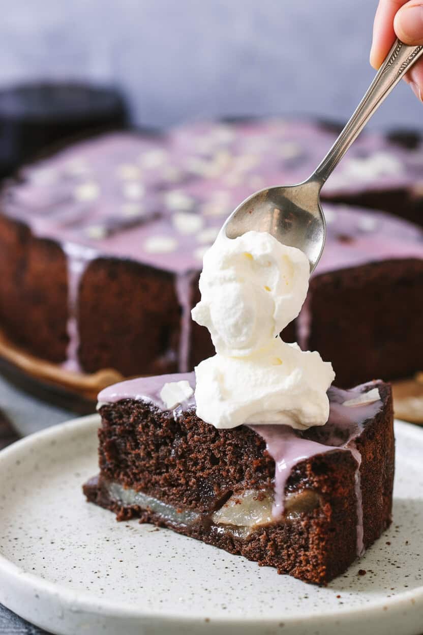 ein Löfffel Sahne wird auf ein Stück Rotweinkuchen mit Birnen gegeben 
