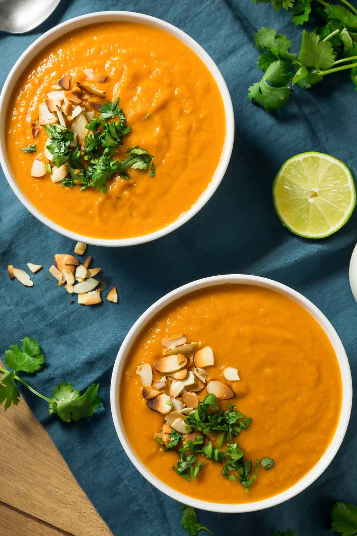 zwei Schalen vegane Süßkartoffelsuppe mit Koriander und gerösteten Nüssen dekoriert