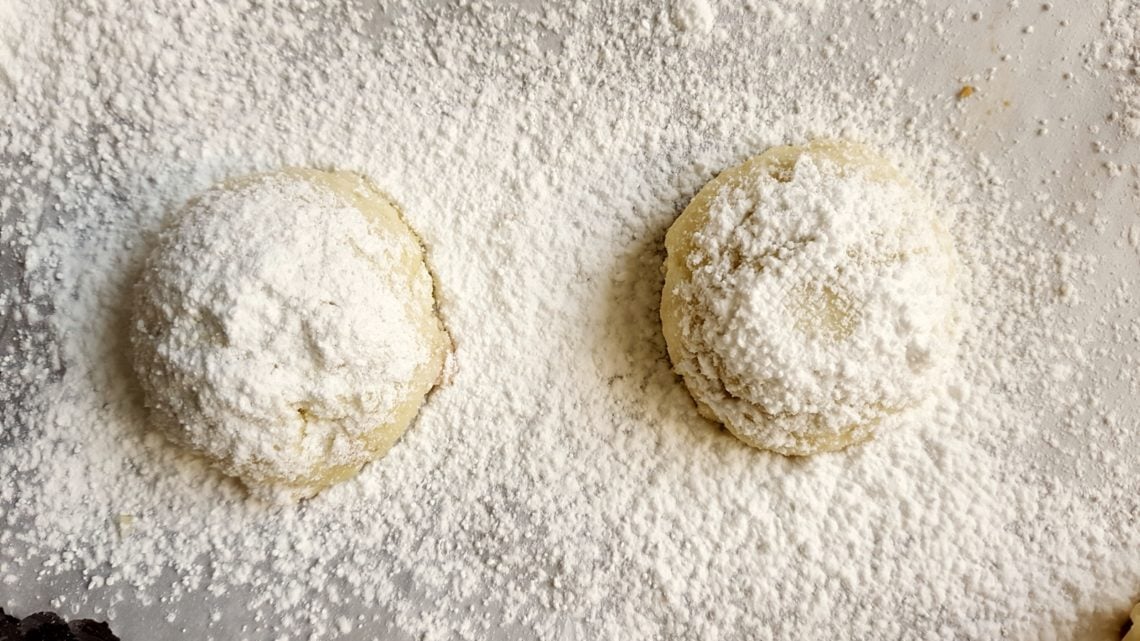 two warm Macadamia and Lime Mexican Wedding cookies being dusted with icing sugar