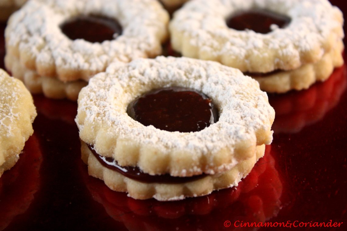 Close up of German Christmas Cookies (Spitzbuben) filled with Black Forest Jam arranged on a red plate