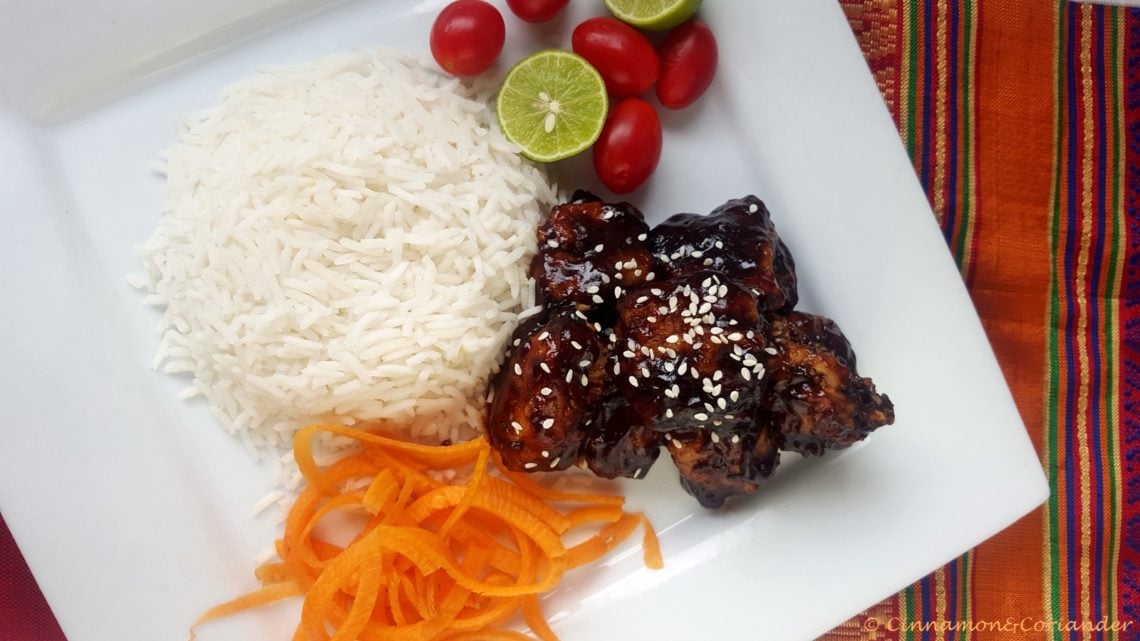 Vegan General Tso Cauliflower sprinkled with sesame seeds on a white plate with a side or rice and veggies