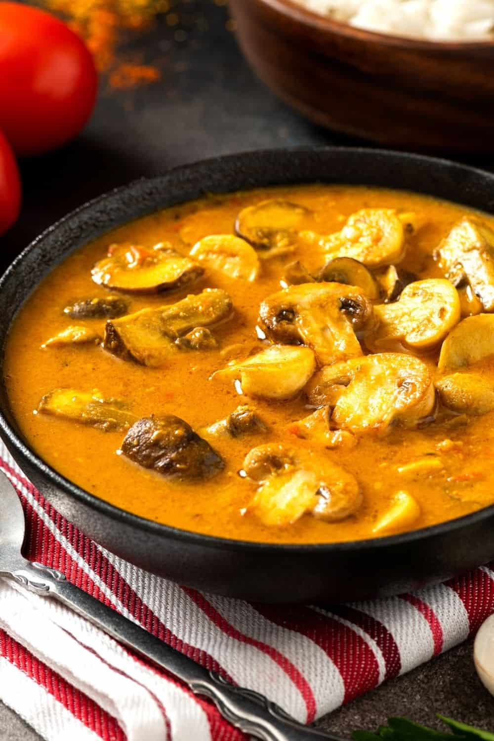 a bowl of vegan mushroom tikka masala with rice in the background.