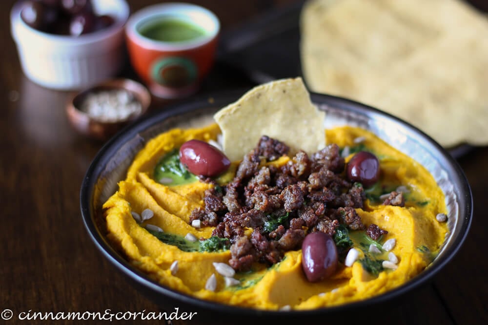 a bowl of healthy roasted kabocha squash hummus with lamb, olives and parsley sauce on top served in a bowl 