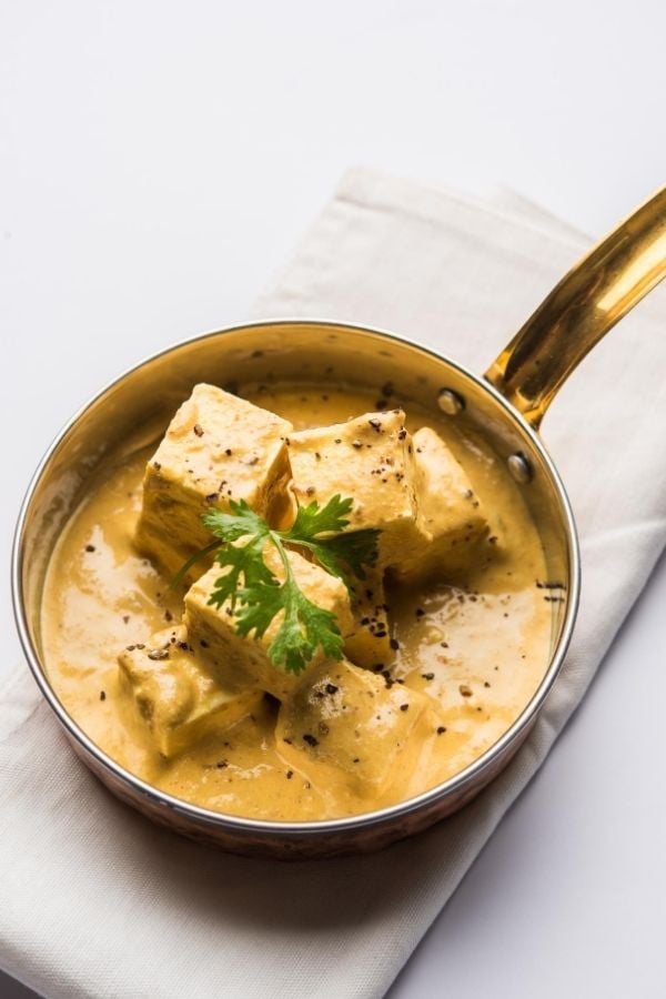 a saucepan with Indian achari paneer masala in yogurt gravy with on a white tablecloth