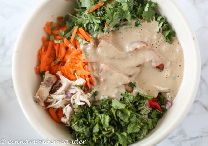 creamy peanut dressing being added to chicken salad in a bowl